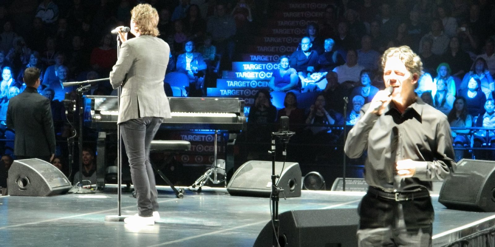 Two vocalists performing on a concert stage under blue light.